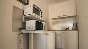 A compact kitchen with white cabinets, a microwave, and a small refrigerator.