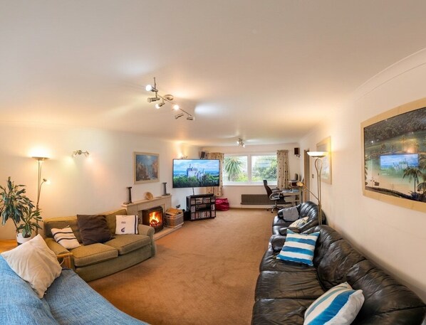 A living room with a fireplace, sofas, a TV, and a large window.