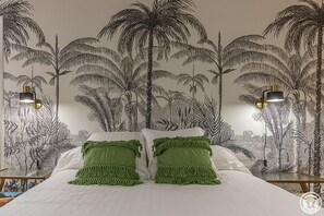 A bedroom with a bed, green pillows, and a wall mural of palm trees.