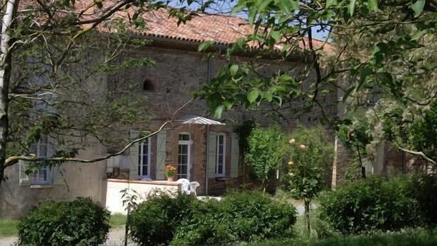 A stone building with a tiled roof, surrounded by greenery and a small garden area.