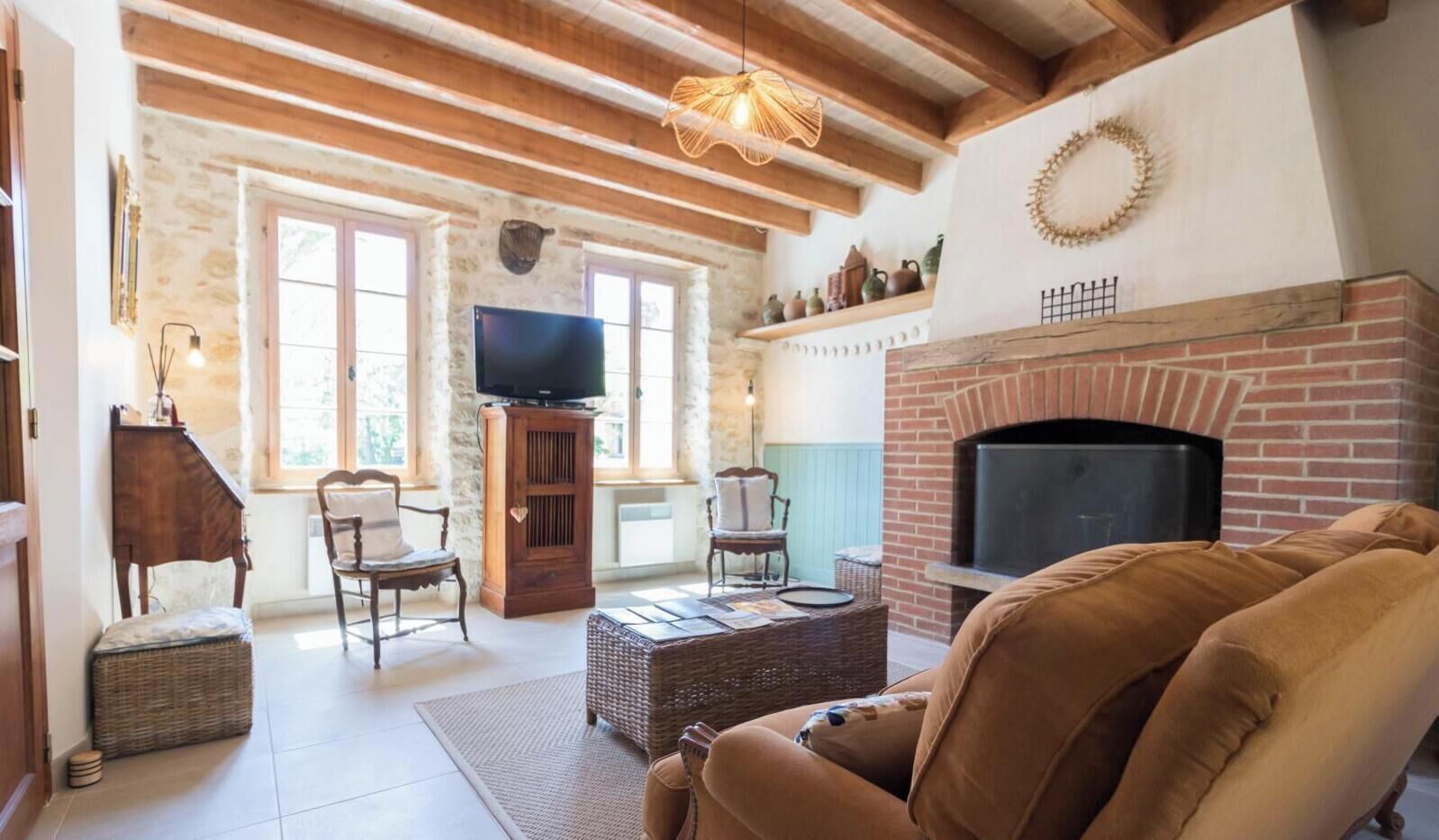 A cozy living room with a fireplace, wooden beams, stone walls, and a television.