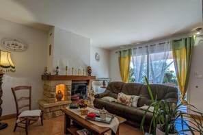 A cozy living room with a stone fireplace, a brown leather sofa, a wooden chair, and a table with various items.