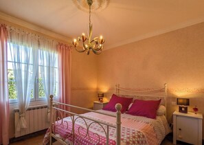 A bedroom with a bed, bedside tables, a chandelier, and a window with curtains.