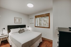 A bedroom with a bed, bedside table, lamp, and a window with a view of trees. - Mt Baker Rim Cabin 24 - Hot Tub, Wifi, Air Conditioning, Sleeps 8 (Deming)