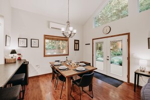 A dining area with a wooden table set for four, a chandelier, and a large window with a view of greenery. - Mt Baker Rim Cabin 24 - Hot Tub, Wifi, Air Conditioning, Sleeps 8 (Deming)