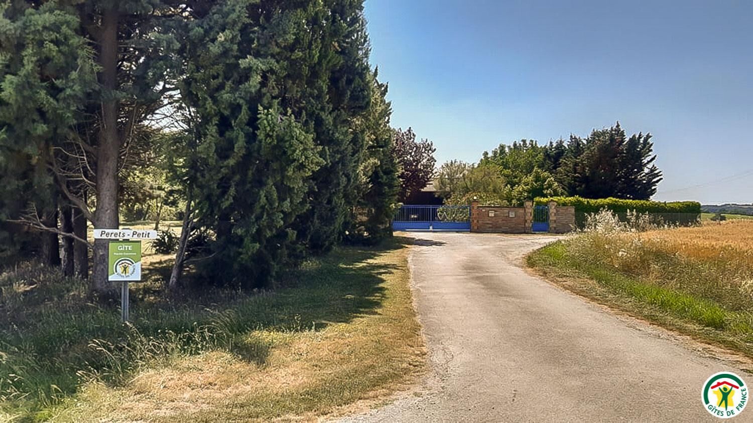 Un camino rural que conduce a una entrada con portón, con un cartel que indica 'Perets - Petit' y 'GITE'.