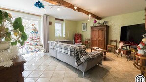 Ein gemütliches Wohnzimmer mit einer Couch, einem Esstisch und einem Fernseher. Im Hintergrund ist ein Weihnachtsbaum zu sehen.