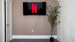 Ein Flur mit an der Wand befestigtem Fernseher, der das Netflix-Logo zeigt, einem Blumentopf und einer Tür.