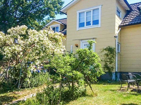 A residential building with a yellow exterior, a visible window, and a small garden area with trees and a pathway.