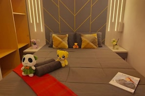 A modern hotel room with a bed, pillows, a red throw, a magazine, and plush toys. - Residence Taman Anggrek By All Property (Jakarta)