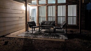 A covered patio area with a brick wall, large windows, and two black chairs on a mat. - Five star ratings! Pet Friendly! Lovely Rockwall home near The Harbor! ⛴️🐡 (Rockwall)