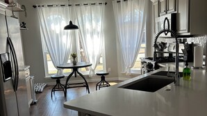 A modern kitchen with a central island, a dining area with a table and chairs, and large windows with sheer curtains. - Five star ratings! Pet Friendly! Lovely Rockwall home near The Harbor! ⛴️🐡 (Rockwall)