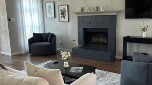 A modern living room with a fireplace, a sofa, a coffee table, and a TV mounted on the wall. - Five star ratings! Pet Friendly! Lovely Rockwall home near The Harbor! ⛴️🐡 (Rockwall)