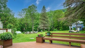A wooden deck with a bench, planters with flowers, and a view of a house and trees in the background. - Art Nouveau Room<br>Large room decorated in the Art Nouveau style with FULL-size bed, en suite bathroom.FREE breakfast. Sleeps 2. (Maplecrest)