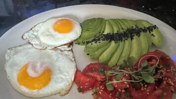 Un piatto con due uova all'occhio, avocado a fette guarnito con semi di sesamo nero, e un'insalata fresca di pomodori e verdure.