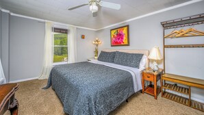 A bedroom with a bed, a nightstand, a lamp, a ceiling fan, a window with curtains, a painting, and a wooden bench. - Fiddler On The Roof Room<br>Room with mountain views, a King-Size bed, en suite bathroom, and FREE breakfast. It sleeps 2. (Maplecrest)