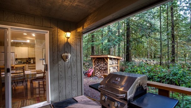 An outdoor patio with a grill, a wooden deck, and a view of a forest.