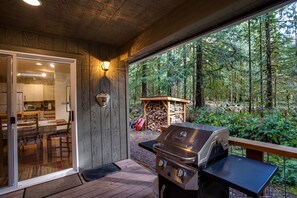 An outdoor patio with a grill, a wooden deck, and a view of a forest. - Glacier Springs Cabin - Wood Stove, Hot Tub, Wifi, Sleeps 8 (Deming)