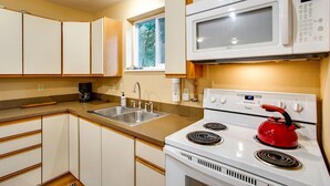 A kitchen with white cabinets, a microwave, a stove, and a red kettle.