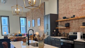 A modern kitchen with a central island, bar stools, a brick wall, and pendant lighting. - Boujee on Third: 2-bedroom condo in Beautiful Downtown Marion  (Marion)
