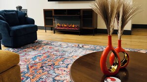 A living room with a flat-screen TV, a blue sofa, a patterned rug, and a coffee table with decorative items. - Boujee on Third: 2-bedroom condo in Beautiful Downtown Marion  (Marion)