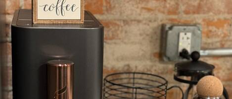 A coffee machine with a sign that reads "BUT FIRST coffee" on a kitchen counter.
