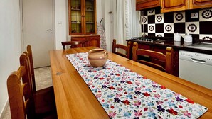 Et spiseområde med et træbord, stole, en bordløber med blomstermønster, en hængende lampe, træskabe og et flisebeklædt bagpanel.