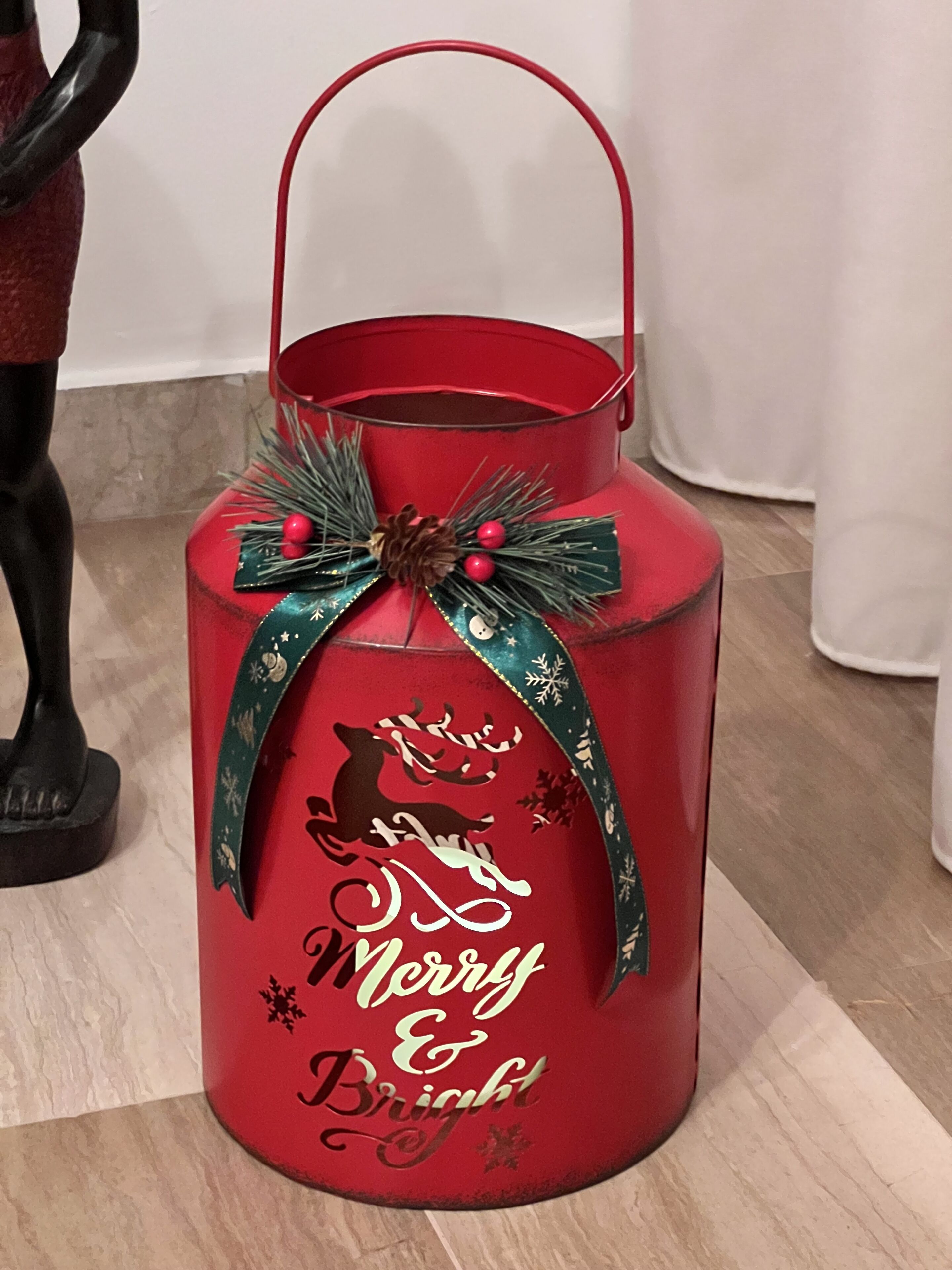 A red lantern with a handle, decorated with a green ribbon and pine branches, and the words "Merry & Bright" written on it.