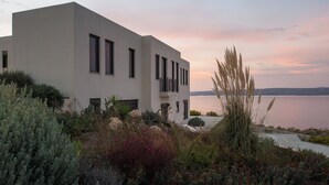 A modern two-story building with a balcony, surrounded by Mediterranean vegetation and overlooking a body of water at sunset. - Villa Peninsula, Luxury accommodation with breathtaking Sea and Mountain views  (Plaka)