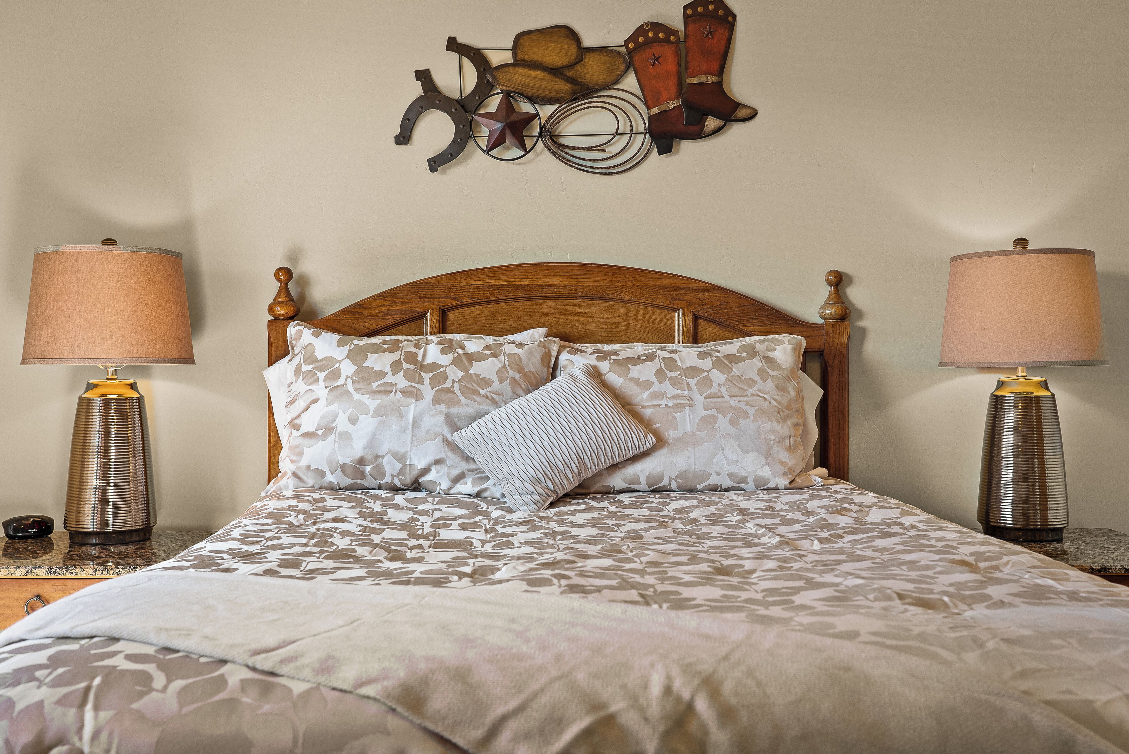 A neatly made bed with patterned bedding, two bedside lamps, and a decorative wall piece above the bed.