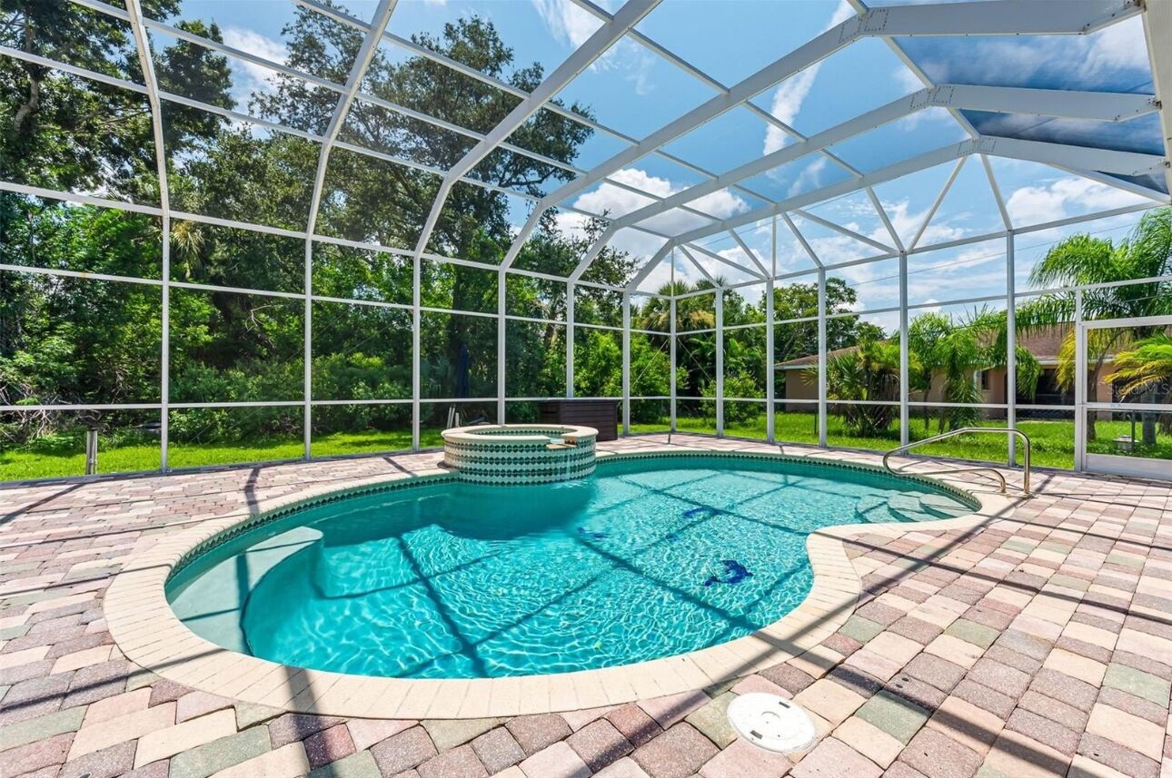A covered swimming pool with a hot tub, surrounded by a brick patio and glass panels.