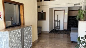 En hotellobby med receptionsdisk, loungeområde, trappe og balkon.