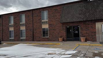 A brick building with a flat roof, large windows, and a door marked "OPEN" indicating a hotel or office. There is snow on the ground, and a yellow curb is visible.