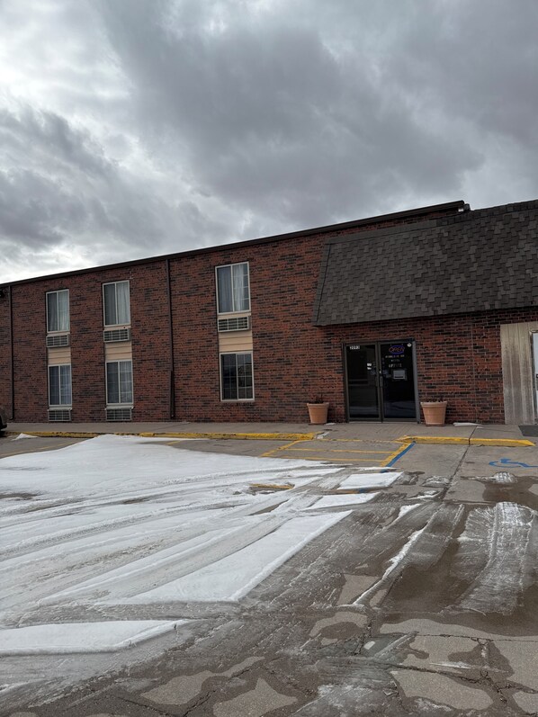 A brick building with a flat roof, large windows, and a door marked "OPEN" indicating a hotel or office. There is snow on the ground, and a yellow curb is visible. - Peddlers Inn Motel (Ulysses)