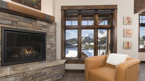 A cozy room with a stone fireplace, a large window with a view of a snowy mountain, and a leather armchair. - Amazing Views - Close to it All! (Big Sky)