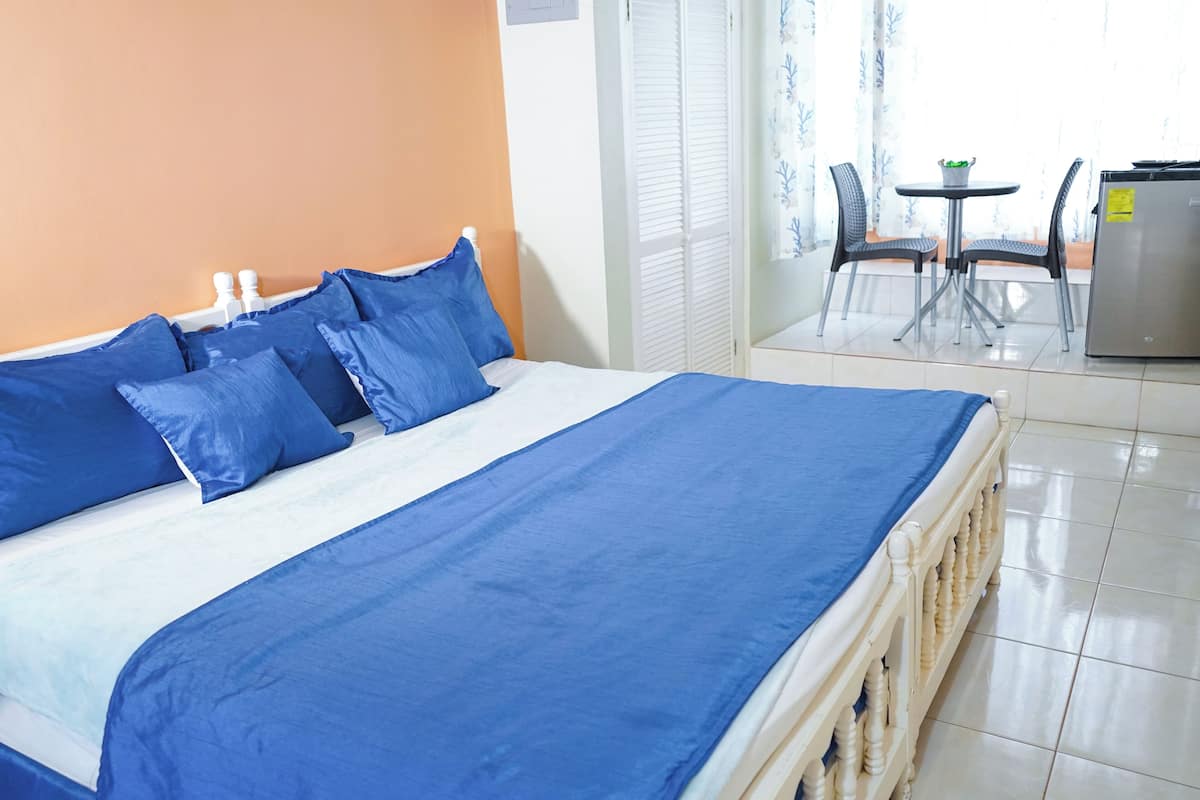 Una habitación de hotel con una cama, un área de comedor con una mesa y sillas, y un refrigerador.