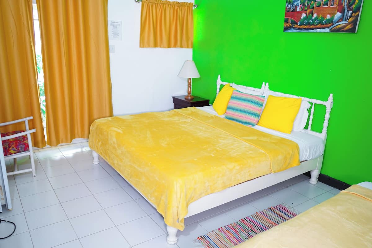 Una habitación con una cama, una mesita de noche, una lámpara, una ventana con cortinas y una pared verde.