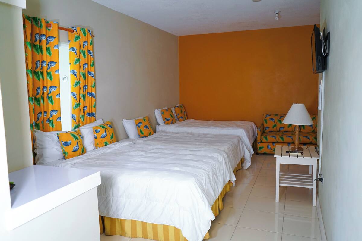 Habitación de hotel con dos camas, una mesita con una lámpara y un televisor montado en la pared.