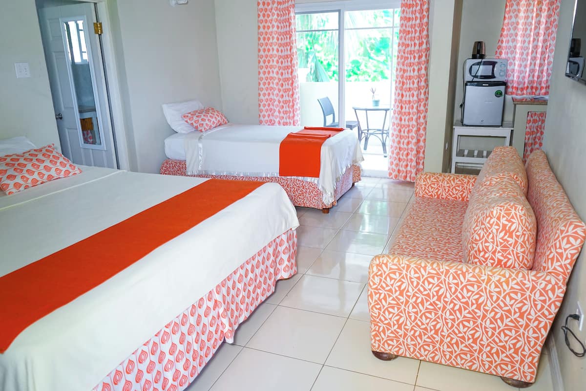 Habitación de hotel con dos camas, un sofá, una mesita, microondas y puerta corrediza de vidrio al exterior.