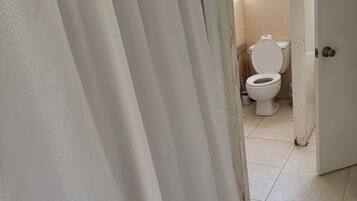 A bathroom with a white toilet, a shower curtain, and a tiled floor.