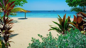Una playa con agua azul cristalina, palmeras y una sombrilla de paja.