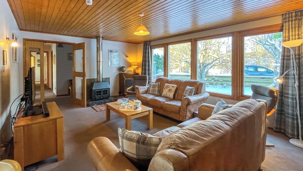 A cozy living room with leather sofas, a fireplace, and large windows offering a view of the outdoors.