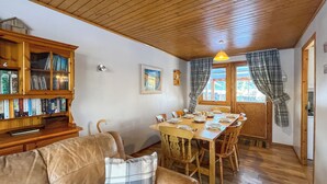 A cozy living room with a wooden ceiling, a dining table set for four, and a leather sofa with a plaid pillow.