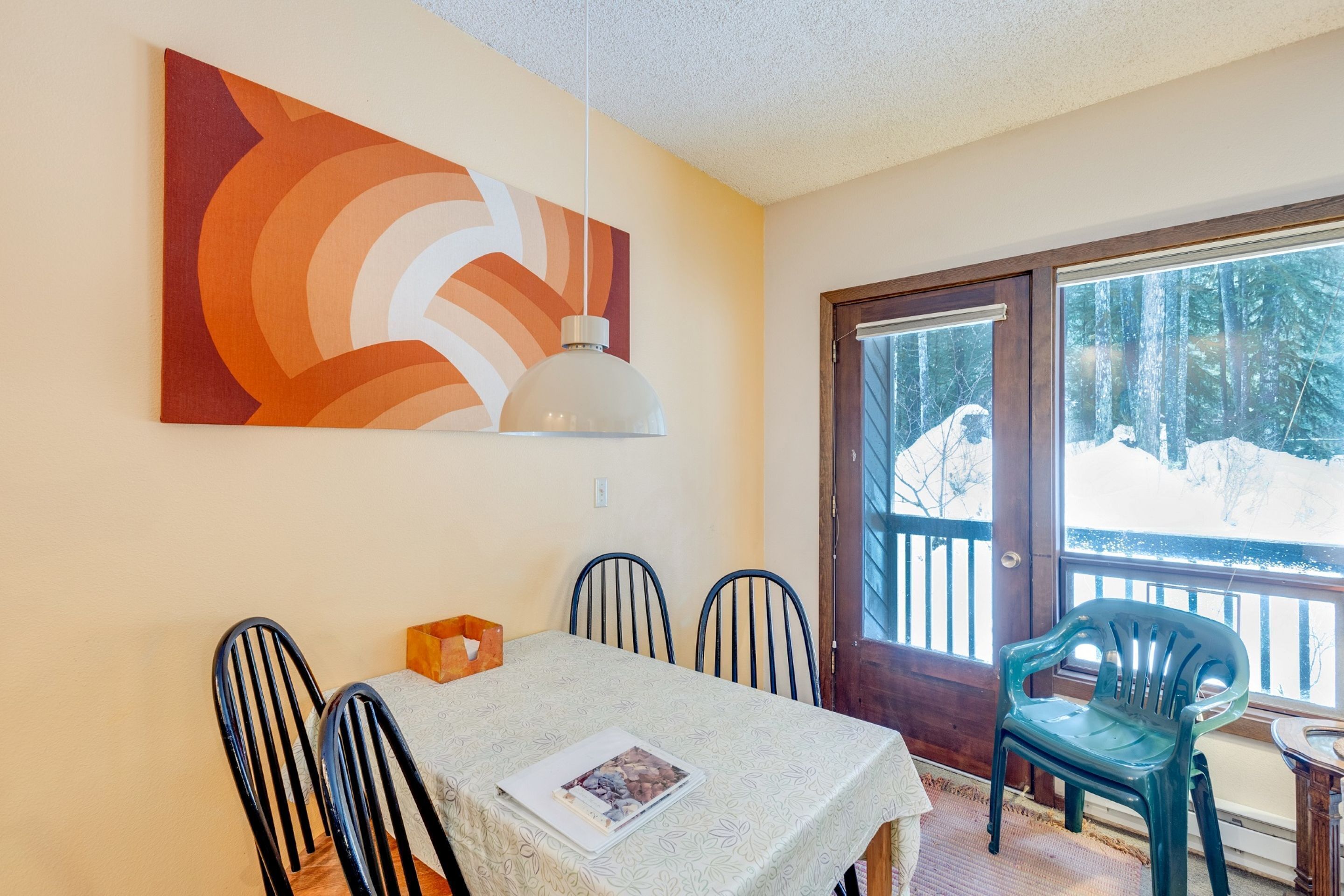 A dining area with a table, chairs, a painting, and a view of a snowy landscape through a glass door.