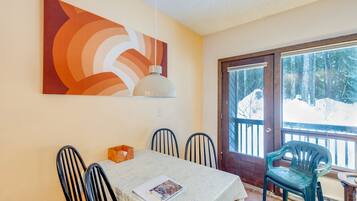 A dining area with a table, chairs, a painting, and a view of a snowy landscape through a glass door.