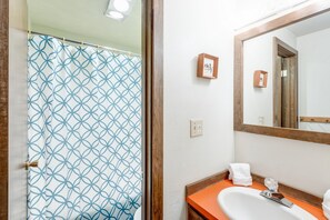 Een badkamer met een wit wastafel, een oranje aanrechtblad, een houten deurkozijn en een douchegordijn met een geometrisch patroon.
