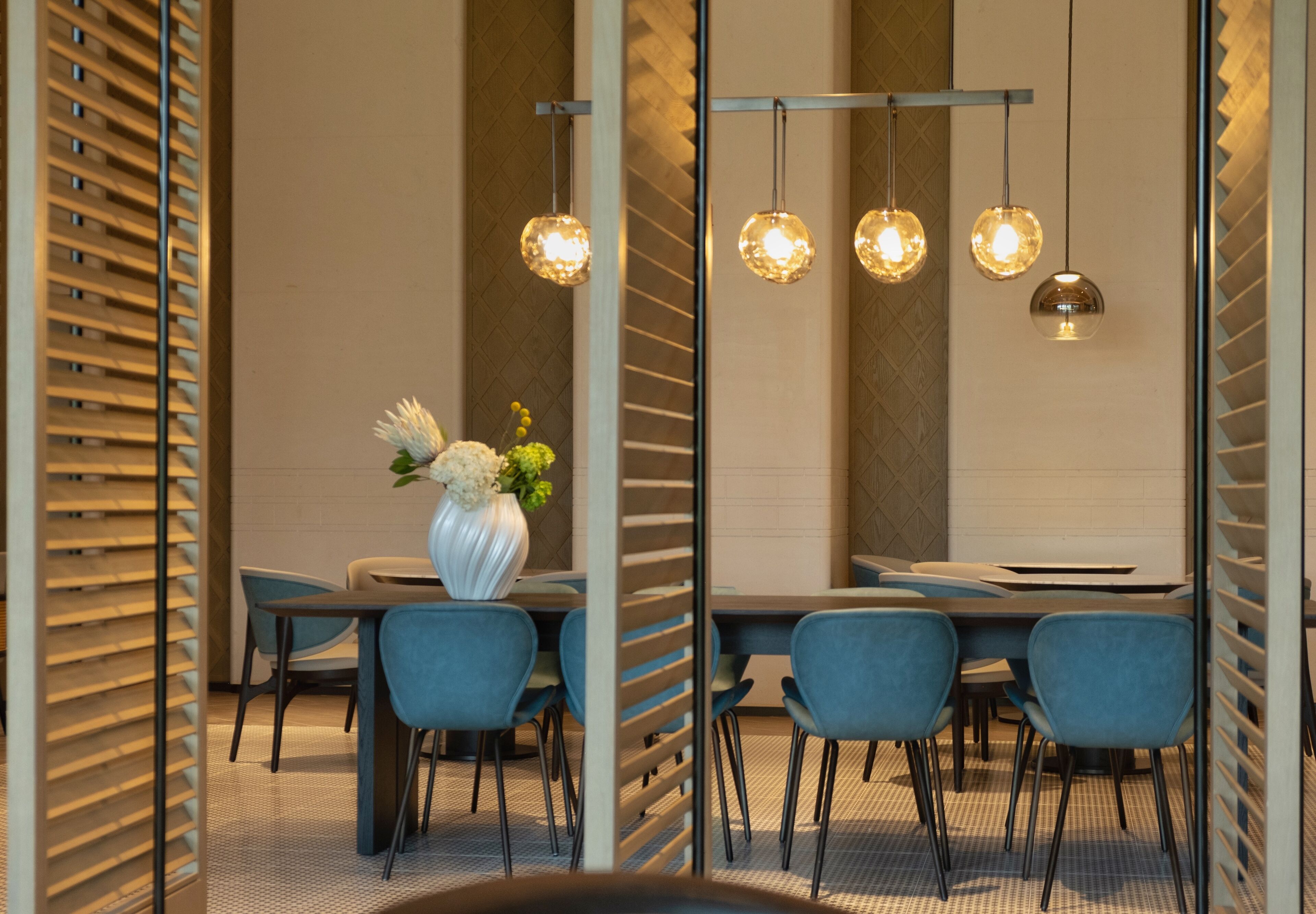A modern dining area with a long table, blue chairs, and hanging spherical pendant lights.