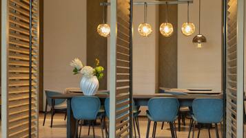 A modern dining area with a long table, blue chairs, and hanging spherical pendant lights.