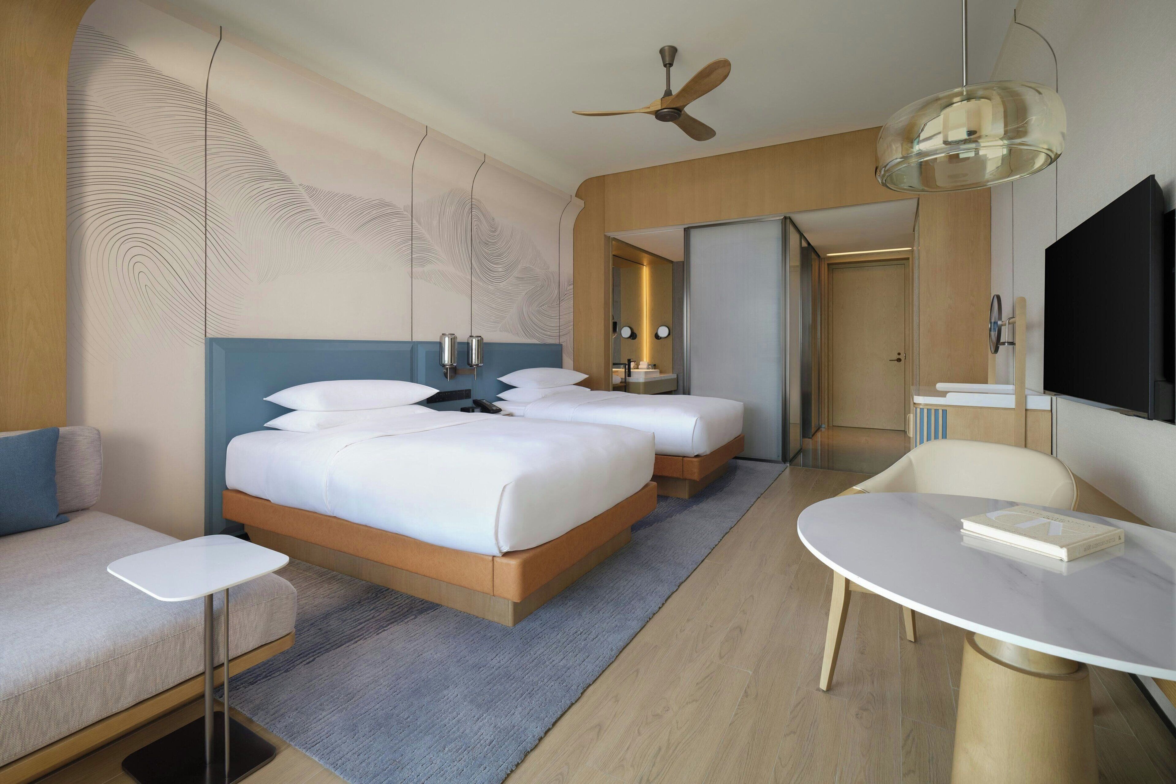 A modern hotel room with a large bed, a small sofa, a dining table, and a TV.