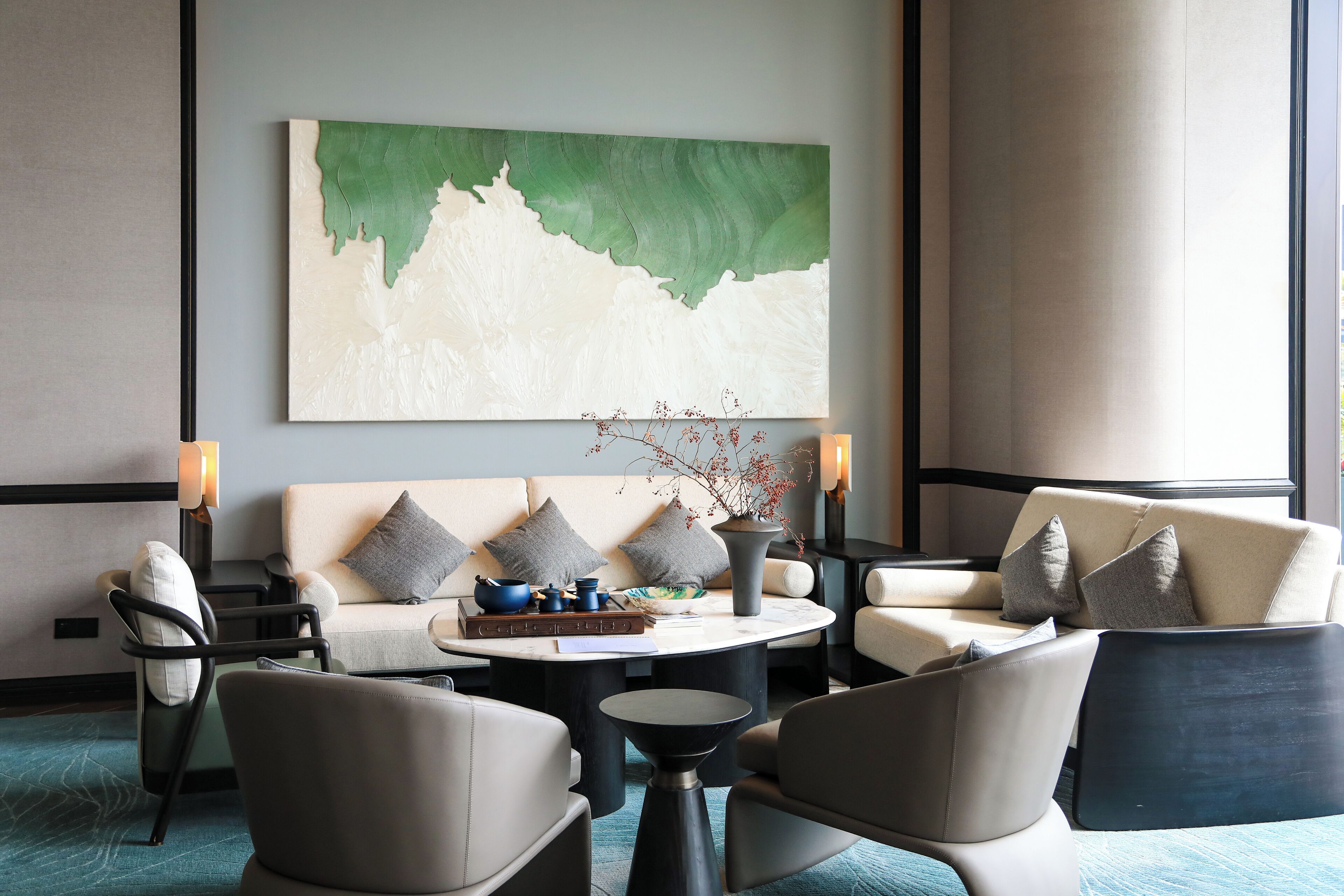 Un área de descanso moderna con sofá, sillones, una mesa de centro y un cuadro abstracto grande en la pared.
